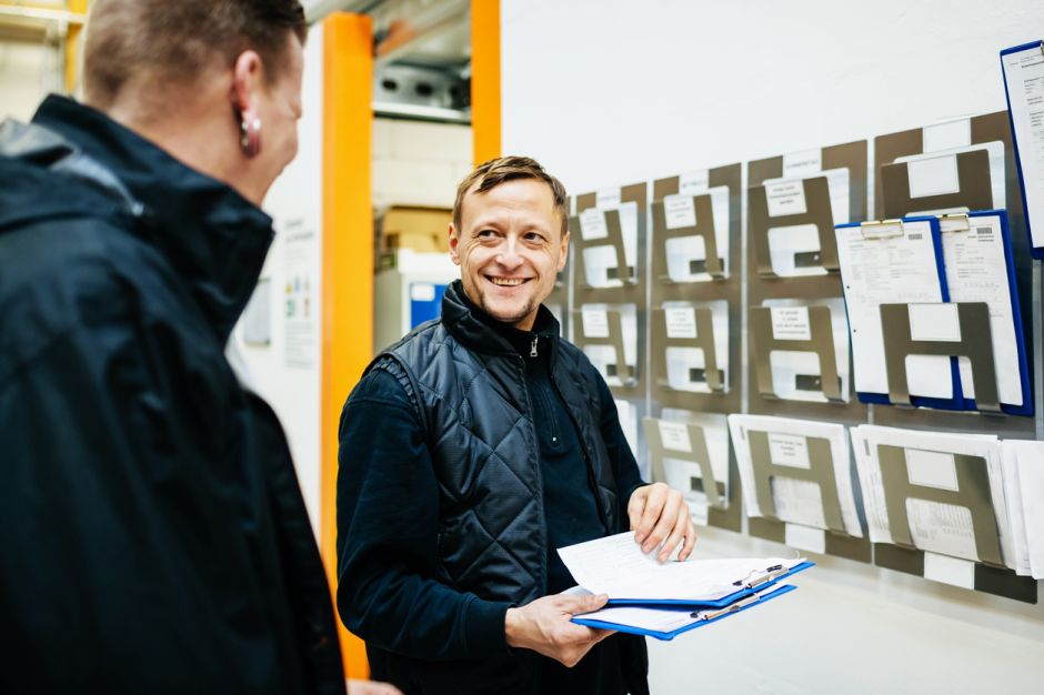 A warehouse manager smiling as he chats to his colleague while organising their workload and schedule for the week.